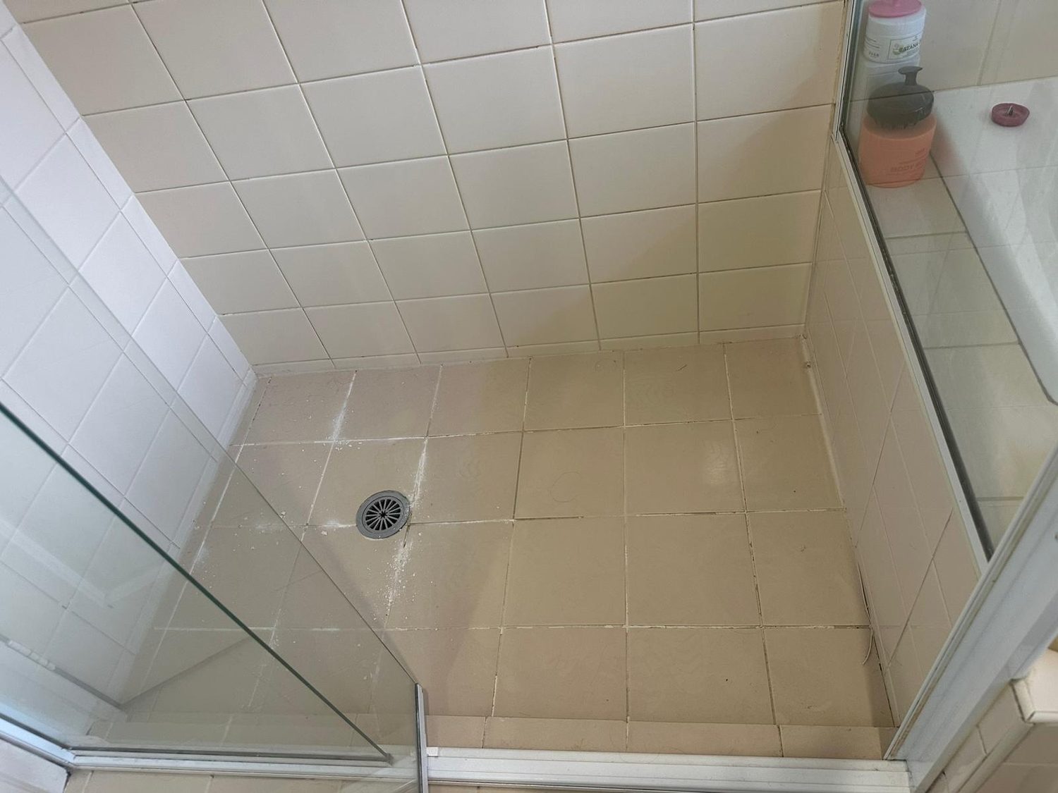Cream-tiled shower with dirty grout before cleaning