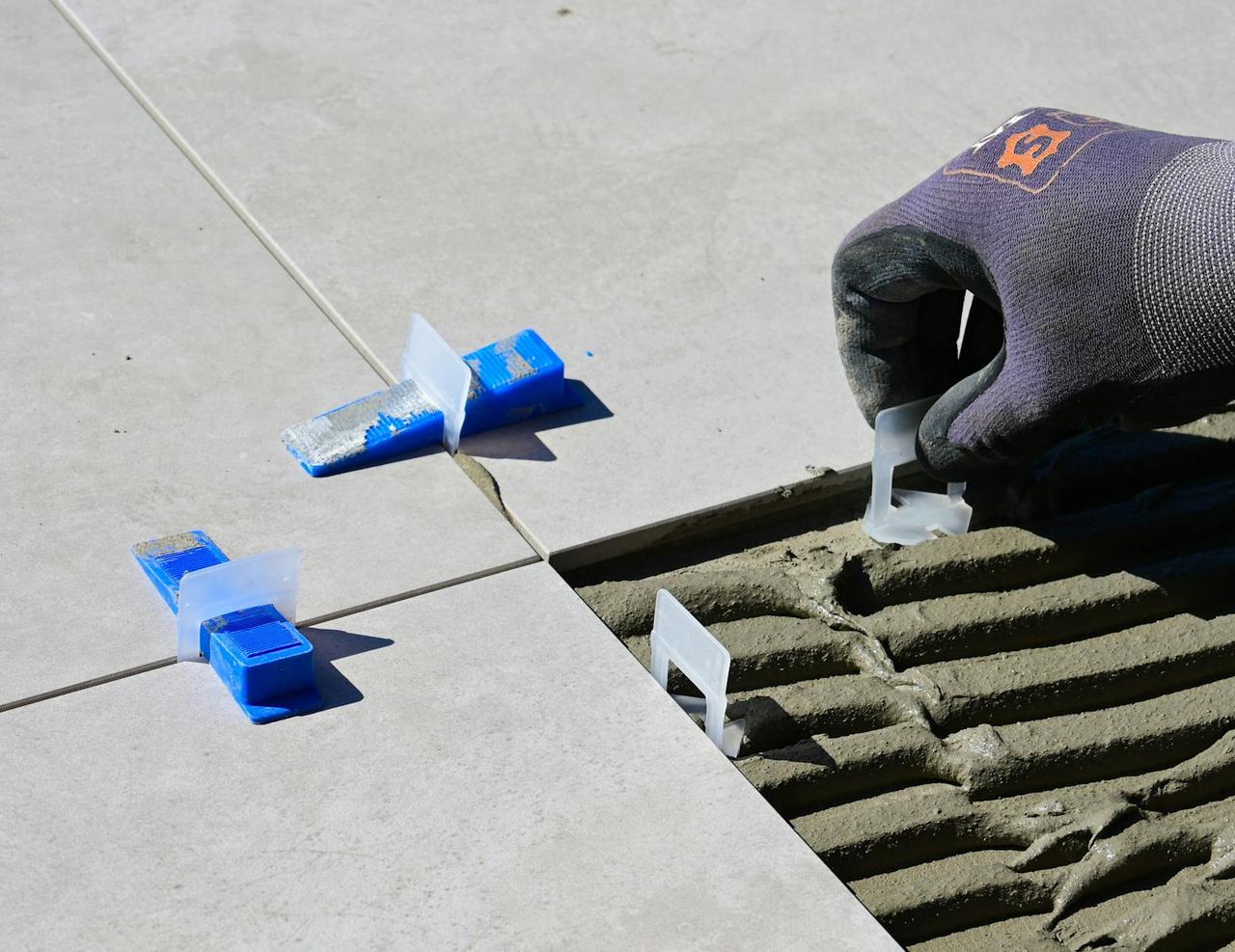 Tiler laying floor tiles with adhesive and a tile levelling system